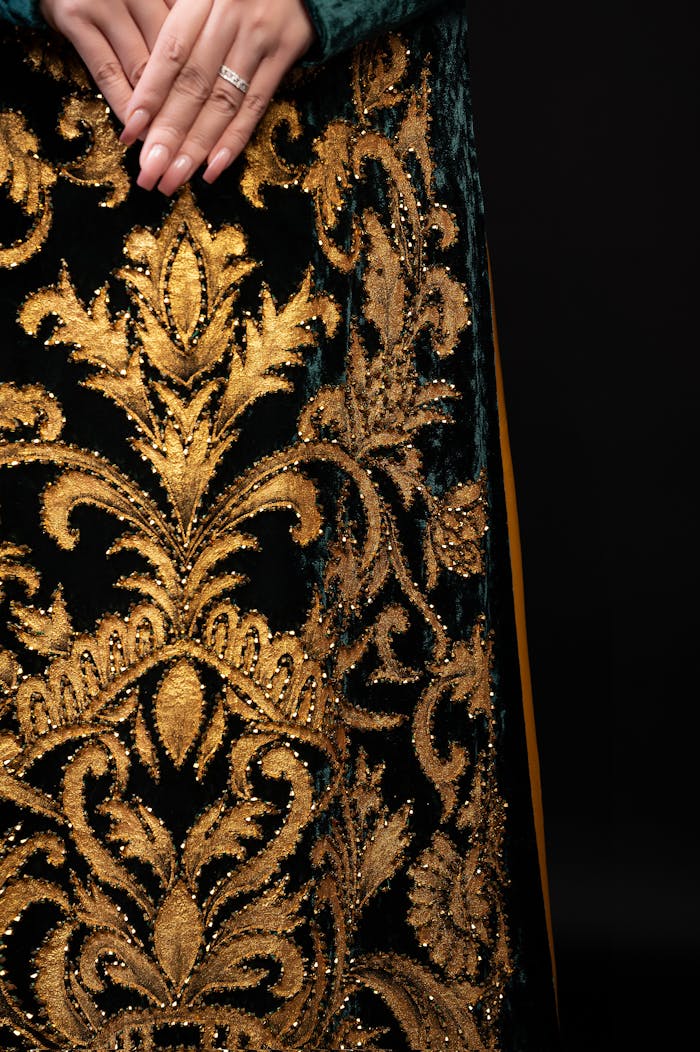 Close-up of an elegant dress with gold embroidery, hands elegantly posed.