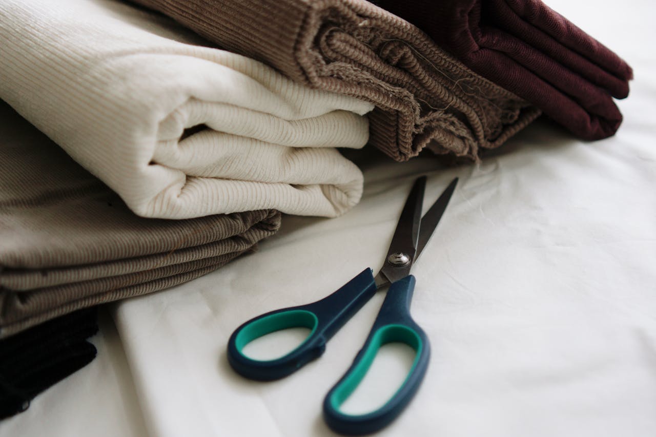 A neatly arranged stack of fabrics with scissors on a white surface, ideal for sewing enthusiasts.