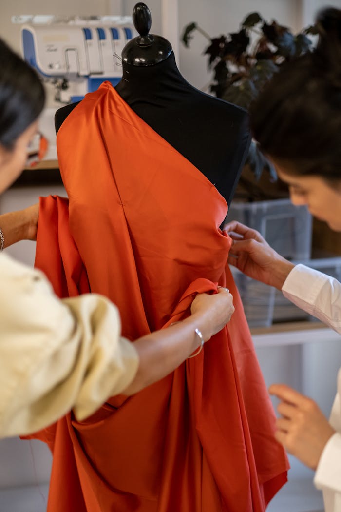 Two designers collaborate in a fashion studio, adjusting fabric on a mannequin.
